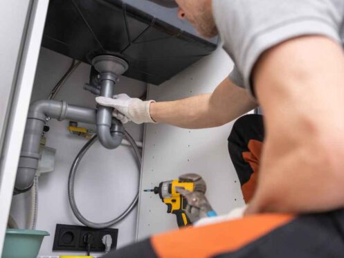 Plumber working on pipes under a sink